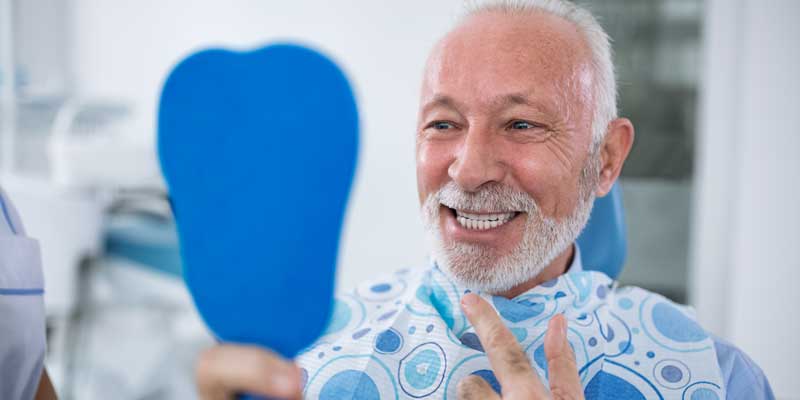 Man Smiling in Mirror With Implant Supported Denture